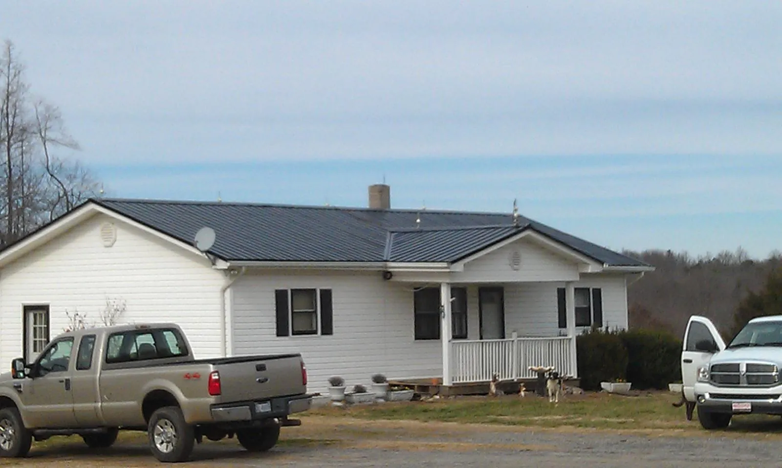 Finished dark metal roof on a white ranch home with work trucks parked in Ardmore